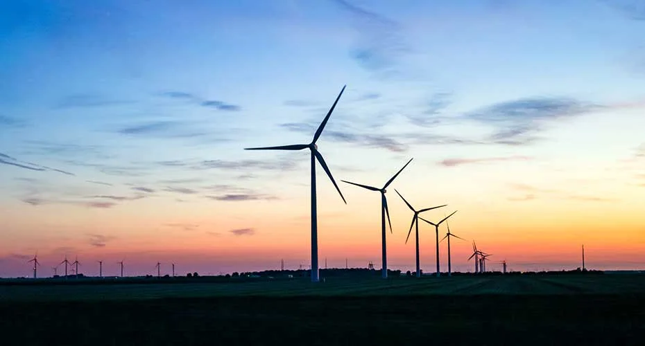 Sunset casts a warm glow on wind turbines standing tall in a peaceful field.