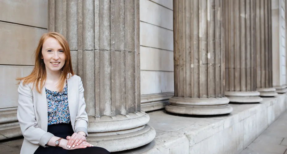 Charlotte, a student, is seated on a bench near elegant columns, reflecting on her studies in a serene environment.