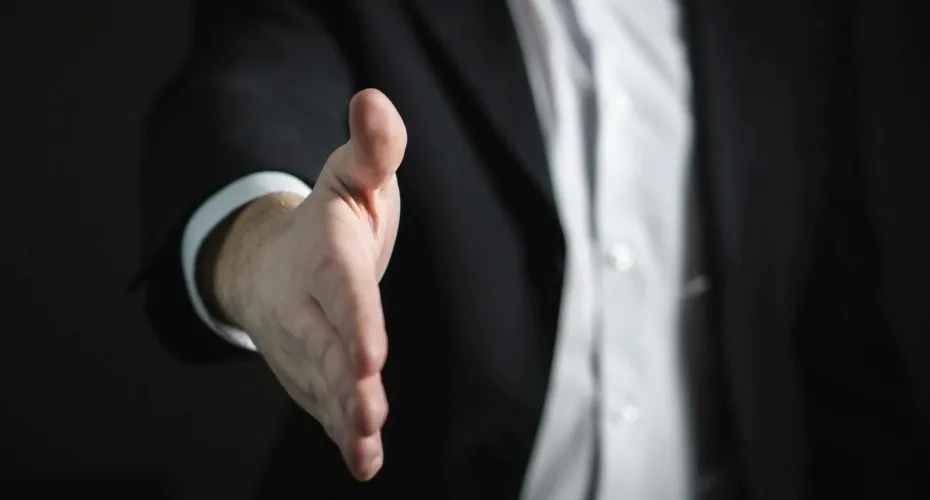 A person in a suit extends his hand forward, inviting or greeting someone.