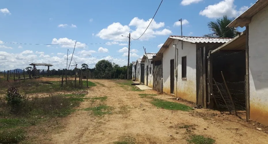 A dirt road lined with small houses and a wooden fence under a clear blue sky.