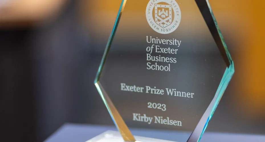 A glass exeter prize award placed on a table against a blue background.