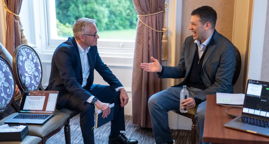 Steve wood and judd kessler engaged in conversation while seated in a room, sharing ideas and thoughts.