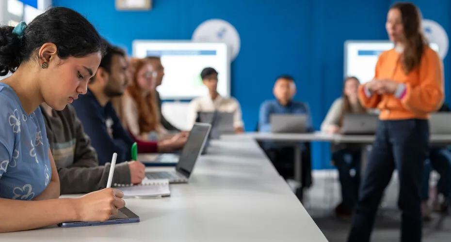 A group of students seated at tables, each using laptops for collaborative work or study.