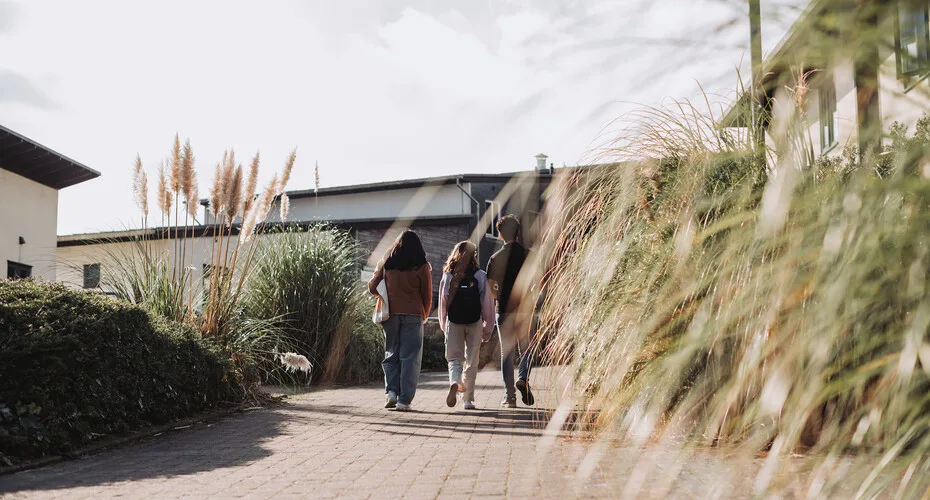 Two students walking along a path in front of a building at penryn campus.