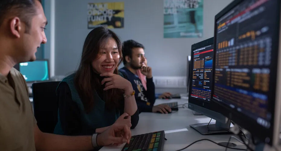 A finance student and lecturer smile while looking at a computer screen together.