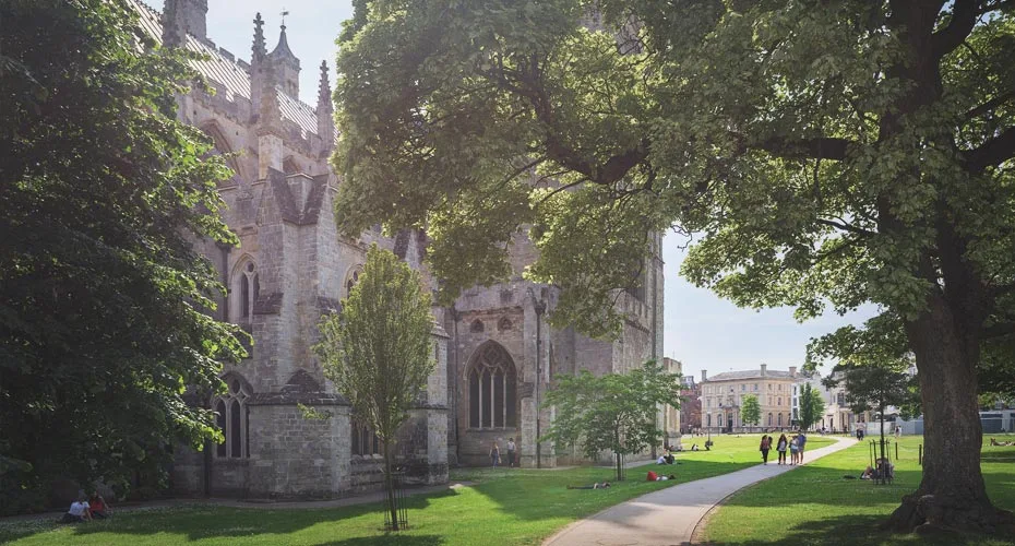 Exeter cathedral stands majestically with a lush green lawn and trees surrounding its impressive structure.