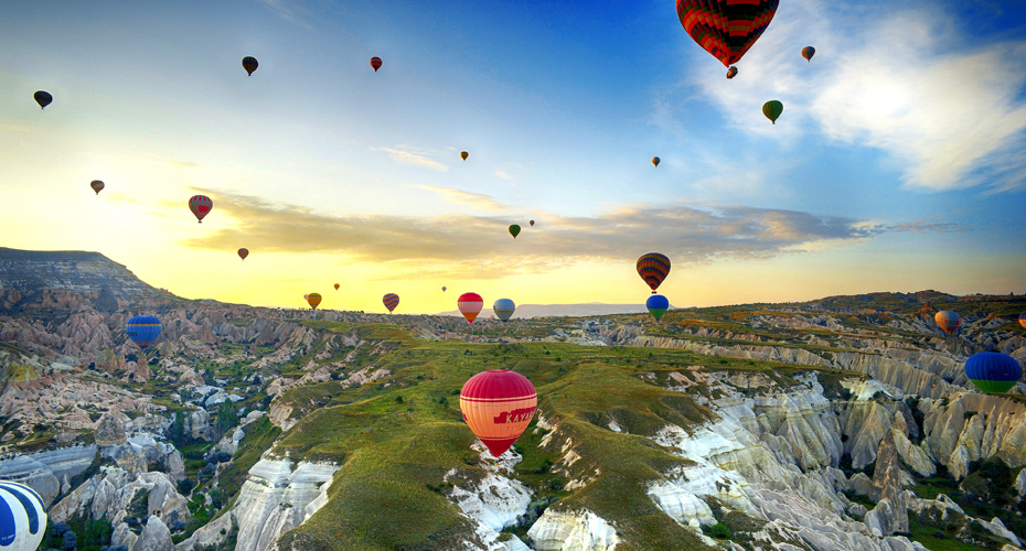 A colorful array of hot air balloons ascends over a majestic mountain landscape under a clear blue sky.